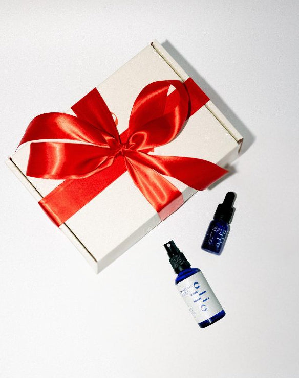 Gift box with a red ribbon and two small bottles of cactus face and signature spritz on a white background